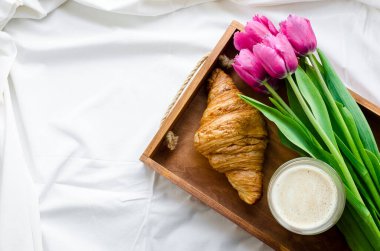 Bir fincan köpüklü kahve ve beyaz yatak balayında pembe laleler. Anneler Günü 'nde, Sevgililer Günü' nde ya da Kadınlar Günü 'nde kahvaltı. Yatakta romantik sabah konsepti sürprizi. Üst Manzara. Boşluğu kopyala.