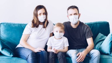 Genç, karantinaya alınmış tıbbi maskeli Coronavirus ailesi. Evde kalma çağrısı salgını durdurur. Kendini izole etmek bir çözüm. Coperid 19 'a dikkat et. Hamile anne, baba ve oğul milenyumu.