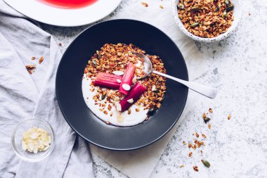 Ev yapımı granola yoğurt ve gri arka planda haşlanmış ravent ile servis edilir. Gurme sağlıklı kahvaltı. Üst görünüm.