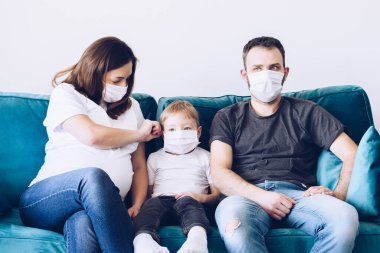 Genç, karantinaya alınmış tıbbi maskeli Coronavirus ailesi. Evde kalma çağrısı salgını durdurur. Kendini izole etmek bir çözüm. Coperid 19 'a dikkat et. Hamile anne, baba ve oğul milenyumu.