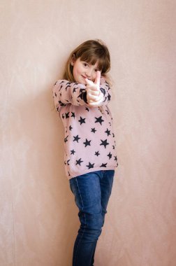 Uzun koyu sarı saçlı, yüzünde sevimli bir gülümsemeyle küçük bir kız gelecekte model olmak için hayatı ve hayalleri seviyor. Onun küçük parmakları son derece dokunaklı. Şık kıyafetler. Pembe arkaplan.