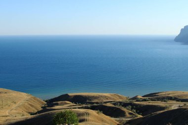 Deniz Burnu. Uçurum, deniz, güneş, açık havada çimen. Denizde tatil. Sakin bir deniz manzarası. Güney doğasının insansız fotoğrafı. Yaz ya da sonbahar turizmi, tepeler ve dağlar
