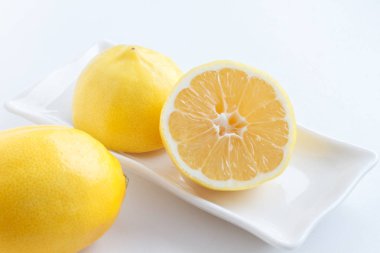 Limon yarım kesilmiş. Tabakta bir limon yanında yalan yalan limon iki yarısı.