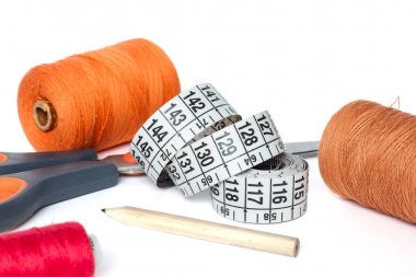 Makas, bir santimetre ve bir kalem. Biriktiricileri iş parçacığı kırmızı, turuncu ve kahverengi. Beyaz bir arka plan üzerinde.