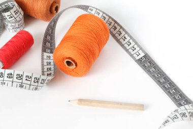 Dikiş aksesuarları: iş parçacığı, bir kalem ve bir santimetre beyaz zemin üzerinde. Turuncu, kahverengi ve kırmızı bobin iplik.