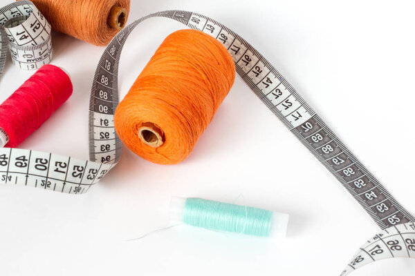 Accessories for sewing: thread and centimetre on a white background. Orange, brown, blue and red bobbin thread.