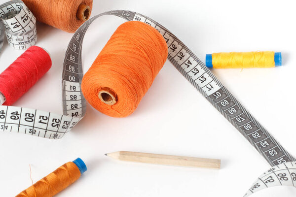 Accessories for sewing: thread, a pencil and a centimeter on a white background. Orange, brown and red bobbin thread.