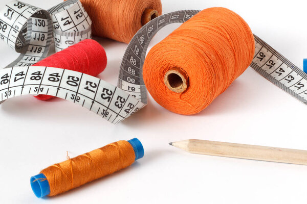 Accessories for sewing: threads, scissors, jeans shorts and centimeter on a blue background. Place for text.