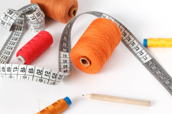 Accessories for sewing: thread, a pencil and a centimeter on a white background. Orange, brown and red bobbin thread.