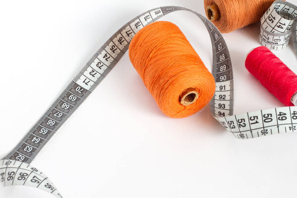 Accessories for sewing: thread, needle and centimetre on a white background. Orange, brown and red bobbin thread.