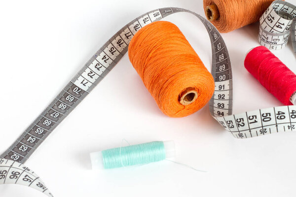 Accessories for sewing: thread and centimetre on a white background. Orange, brown, blue and red bobbin thread.