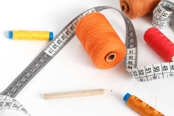 Accessories for sewing: thread, a pencil and a centimeter on a white background. Orange, brown and red bobbin thread.