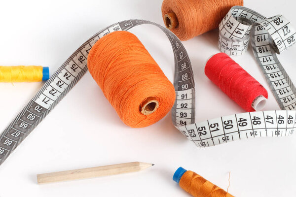 Accessories for sewing: thread, a pencil and a centimeter on a white background. Orange, brown and red bobbin thread.