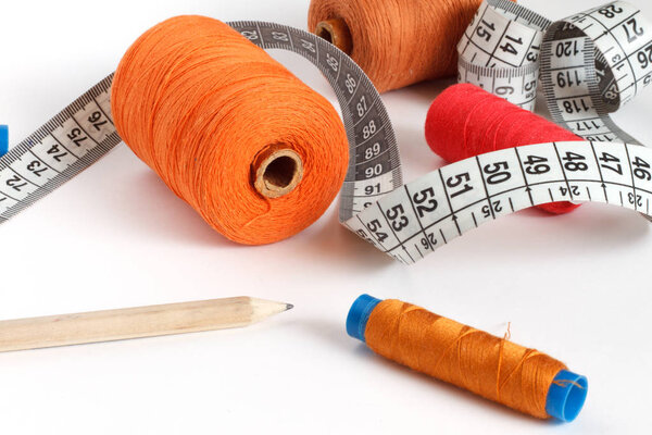 Accessories for sewing: threads, scissors, jeans shorts and centimeter on a blue background. Place for text.