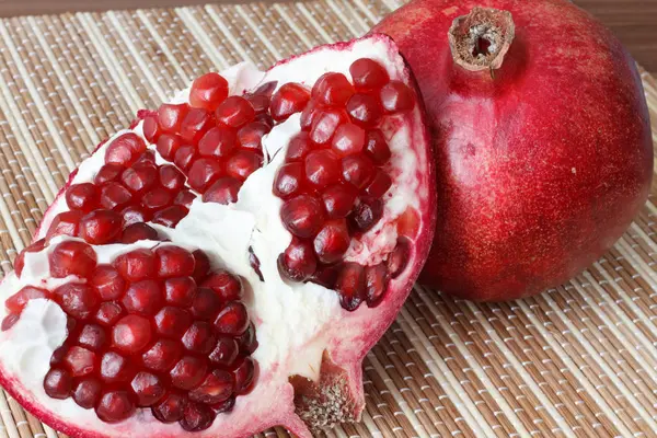 Eine ganze reife Granatapfelfrucht liegt neben den Granatapfelscheiben. leuchtend reife rote Granatapfelkerne. — Stockfoto