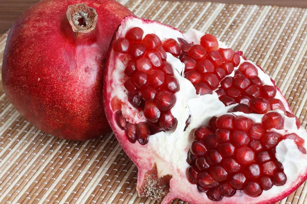 En helt mogen granatäpple frukt ligger intill skivor av granatäpple. Ljusa mogna röda granatäpplekärnor. — Stockfoto