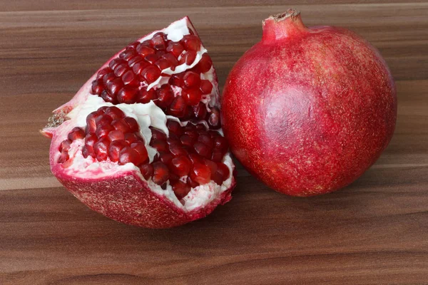En helt mogen granatäpple frukt ligger intill skivor av granatäpple. Ljusa mogna röda granatäpplekärnor. — Stockfoto