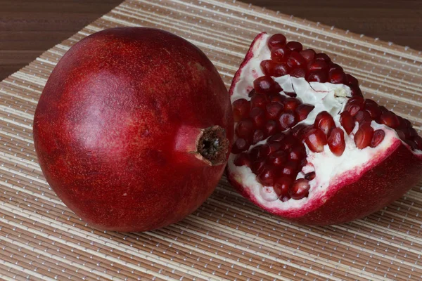 Eine ganze reife Granatapfelfrucht liegt neben den Granatapfelscheiben. leuchtend reife rote Granatapfelkerne. — Stockfoto