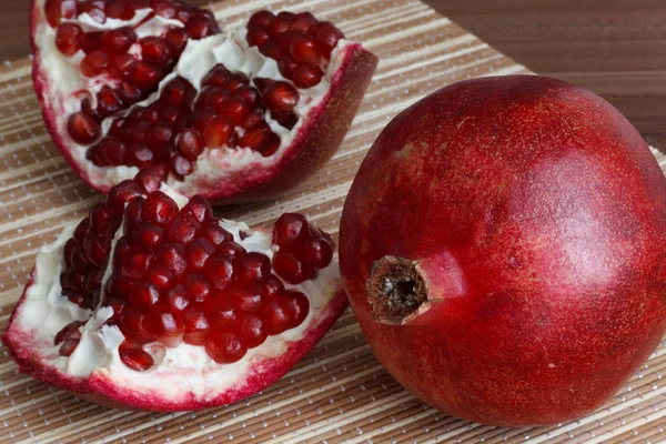 Eine ganze reife Granatapfelfrucht liegt neben den Granatapfelscheiben. leuchtend reife rote Granatapfelkerne. — Stockfoto