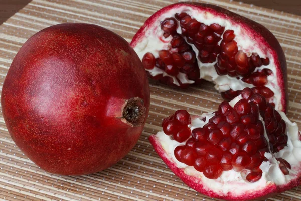 Целый спелый плод граната лежит рядом с ломтиками граната. Ярко зрелые семена красного граната . — стоковое фото