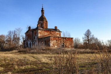 Kırmızıya boyanmış Ortodoks kilisesi, sonbahar otlağının ortasında duran mavi gökyüzüne karşı.