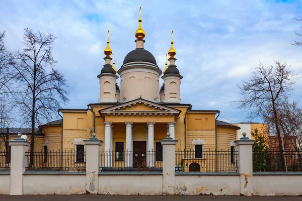 Orthodox church of yellow color with golden domes and white columns against a cloudy sky