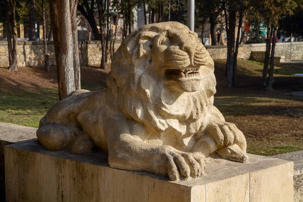 Stone statue of a lion holding a snake in his left paw