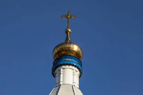 The dome of an Orthodox church with a cross on a background of blue sky. Dome and cross of gold color.