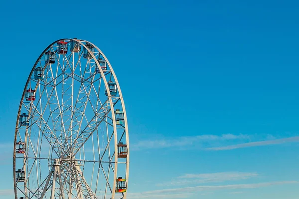 Mavi gökyüzünün arka planında çok renkli kamaraları olan yüksek dönme dolap.
