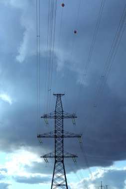 Bulutlu bir gökyüzüne karşı giden elektrik kablolarıyla elektrik hattının çelik direği