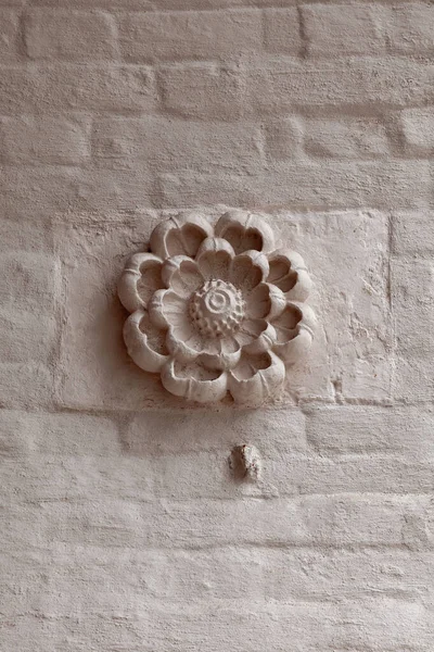 Fragment of the wall of an old church with decoration in the shape of a plaster flower lit by the setting sun