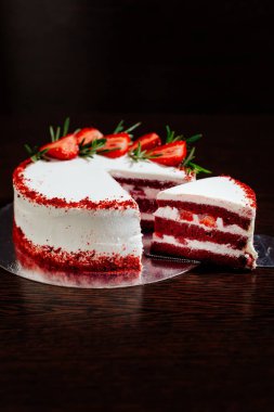 Koyu arkaplanda kırmızı kadife kek. Çilek parçaları ve biberiyeyle süslenmiş beyaz tereyağlı kırmızı kadife kek. Kesikte kırmızı kadife pasta.