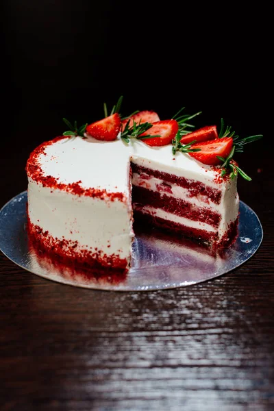 Red velvet cake on a dark background. Red velvet cake in white butter cream decorated with strawberry pieces and a sprig of rosemary. Red velvet cake in the cut.