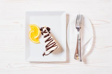 Yanında çikolata konservesi olan beyaz bir tabakta ev yapımı peynirli kek iki dilim portakaldır. Hepsi beyaz ahşap arka planda