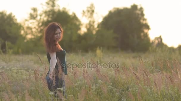 Feliz joven mujer caminando en un campo y acariciando las plantas con su mano . — Vídeo de stock
