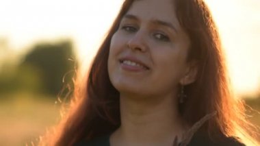 Güzel model kız kot pantolon ve güneş ışığı alan bir yeşil forması giymiş. Yakın çekim. Gülümsüyor.