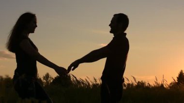 Aşık çerçevede görüntülenir. Birbirlerine yaklaşım ve el ele. Günbatımı gökyüzü arka plan üzerinde.