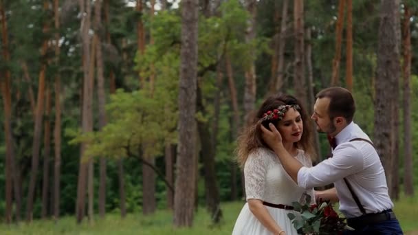 Sposa felice di lusso e sposo elegante, seduto su un tronco in una foresta estiva. Lo sposo accarezza delicatamente la sposa . — Video Stock