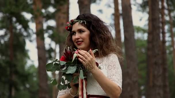 Hermosa novia en un vestido vintage con ramo de colores de flores frescas de cuervo en su cabeza al aire libre en el bosque de verano . — Vídeo de stock