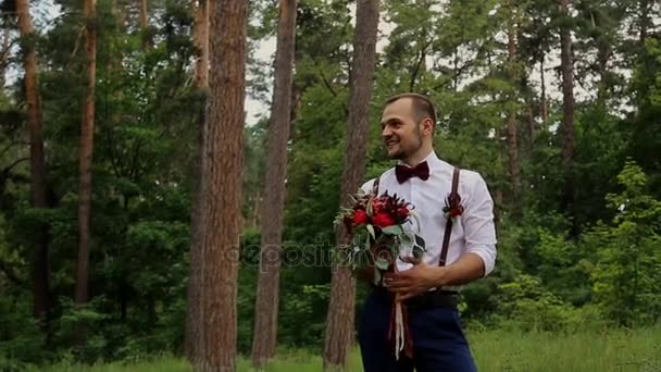 Porträtt bröllop brudgummen poserar med buketten i hand i en sommar skog. — Stockvideo