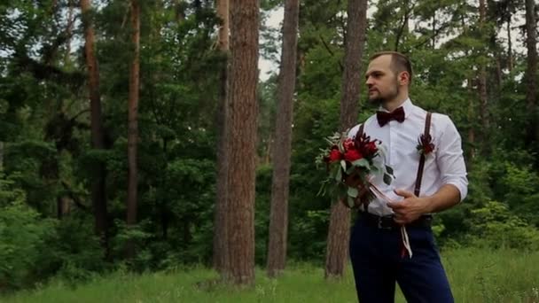 Gyönyörű fiatal csípő pár göndör menyasszony erdő pózol. A vőlegény tart a kezében egy gyönyörű csokor — Stock videók