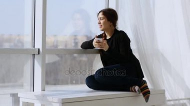 Hoş bir telefon tarafından şaşırtılan genç bir kadın. Pencerede otururken