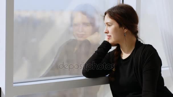 Una joven encantadora mirando curiosamente por la ventana. Giros mirar a la cámara y sonreír — Vídeos de Stock