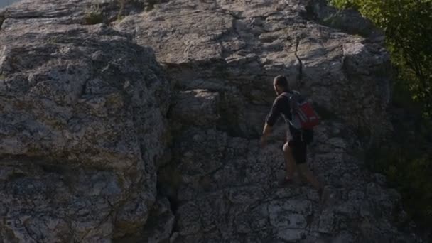 Sommar vandring i bergen. En ung man klättrar på berget. Höjer händerna i ett tecken på seger över sina rädslor och svårigheter — Stockvideo
