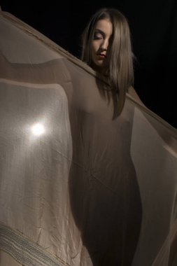 Güzel genç bir kadın ince bir şalının arkasında saklanıyor.