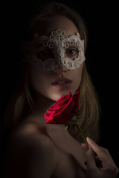 Portrait of a shy girl wearing mask and red rose on black background