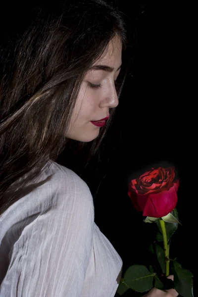 Uzun saçlı, kırmızı gül siyah arka plan üzerine poz ile genç kız
