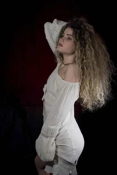 巻き毛とポーズを黒と赤の背景に白いドレスの女性 — ストック写真