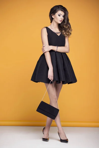 Mooie jonge vrouw in een elegante zwarte jurk op een gele achtergrond — Stockfoto