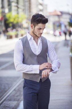 Yakışıklı genç zarif şehirde yürürken saatine bakarak giyinmiş
